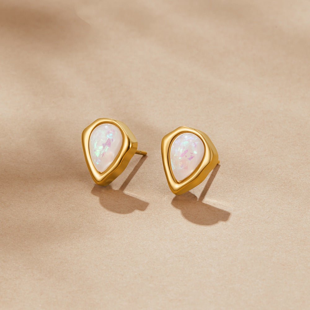 Lily Opal Stud Earrings, a pair of teardrop studs lying on beige fabric, pearly opal centres