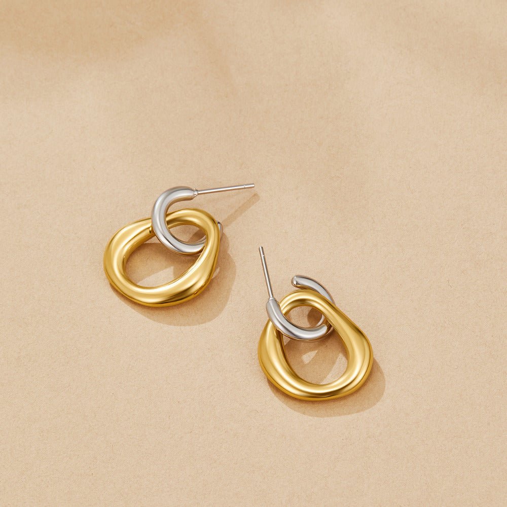 Lola Layered Drop Hoop Earrings, a pair of earrings lying flat on a beige surface, gold loops with silver half-hoops