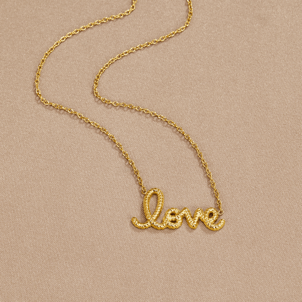 "Love" Pendant Necklace, laid flat on beige fabric, gold script word pendant on chain