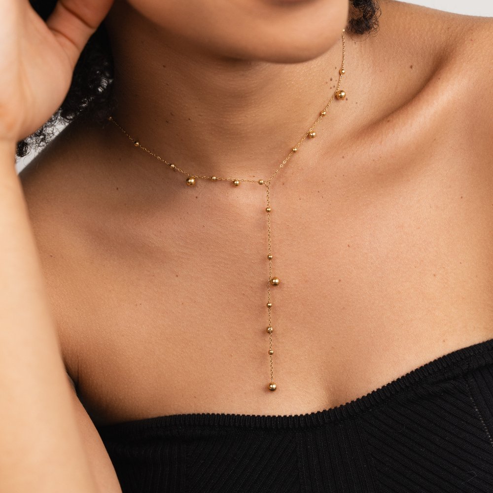 Lovi Gold Beads Tassel Necklace, worn on a neck over a black ribbed top, gold beads along the chain