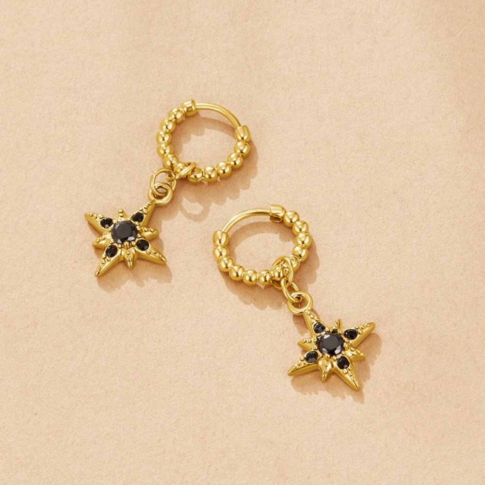 Midnight Luxe Drop Hoop Earrings, pair of gold hoops with star charms set with black stones, on beige