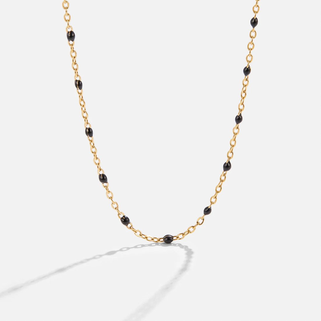 Mila Black Bead Necklace, gold chain necklace with black enamel beads, laid on a light background
