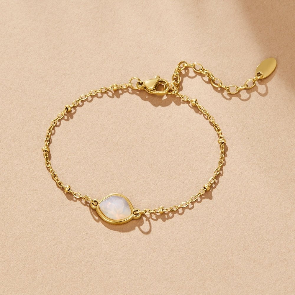Moonstone Charm Bracelet, laid flat on a beige surface, gold chain with pale opal stone