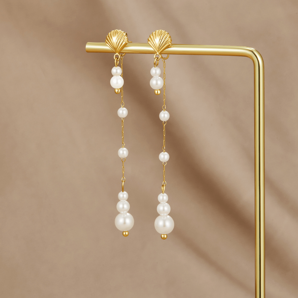 Neesa Pearl Tassel Earrings, hanging on a gold display rod, shell tops with pearl drops