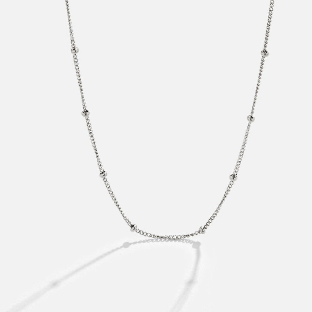 Niyah Bead Silver Chain Necklace, laid out on a light grey surface, silver chain with evenly