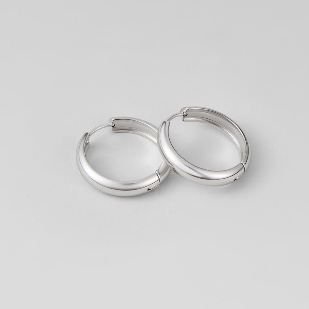 Nona Classic Silver Hoop Earrings, pair of polished silver hoops lying flat on a grey surface