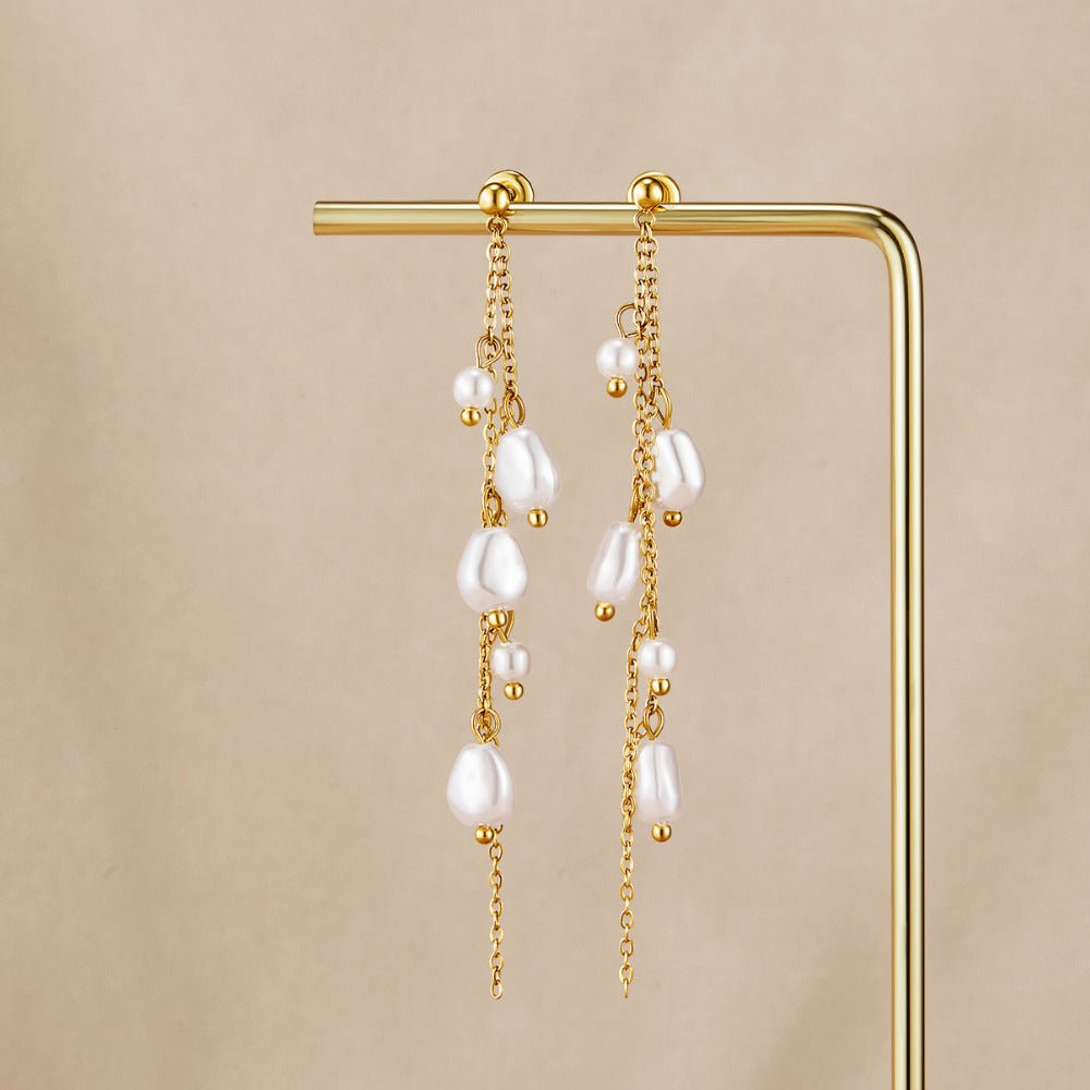 Penelope Pearl Drop Earrings, pair of earrings hung on a gold display stand, against beige fabric