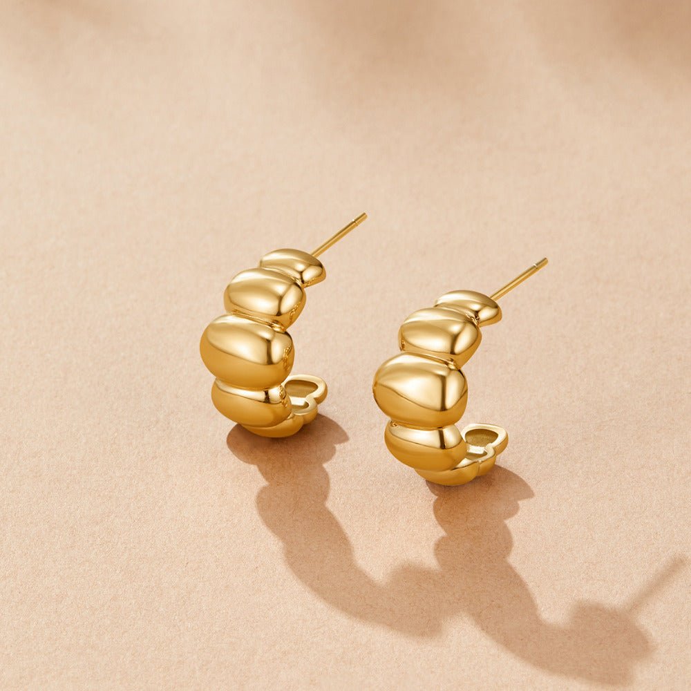 Rene Gold Puff Earrings, pair of glossy gold hoop earrings on a peach surface, casting shadows