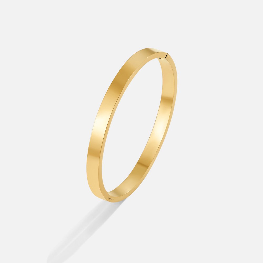 Rina Gold Bangle, standing upright on a light grey surface, polished gold with a hinge