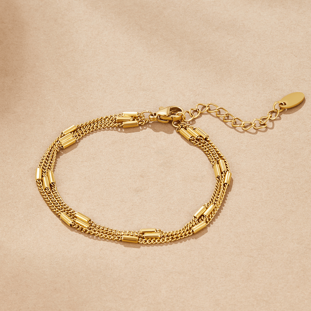 Sabina Triple Layered Bracelet, laid flat on beige paper, gold multi-strand chain with tube