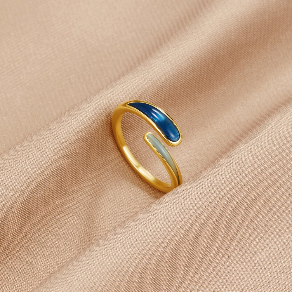 Safira Blue Wrap Ring, lying on a beige satin cloth, gold band with blue and pale enamel