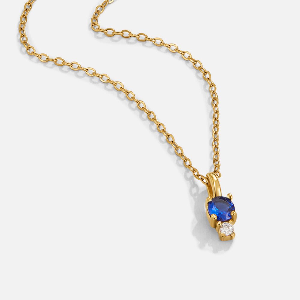 Sapphire Drop Pendant Necklace, gold chain necklace lying flat with blue and clear stone pendant