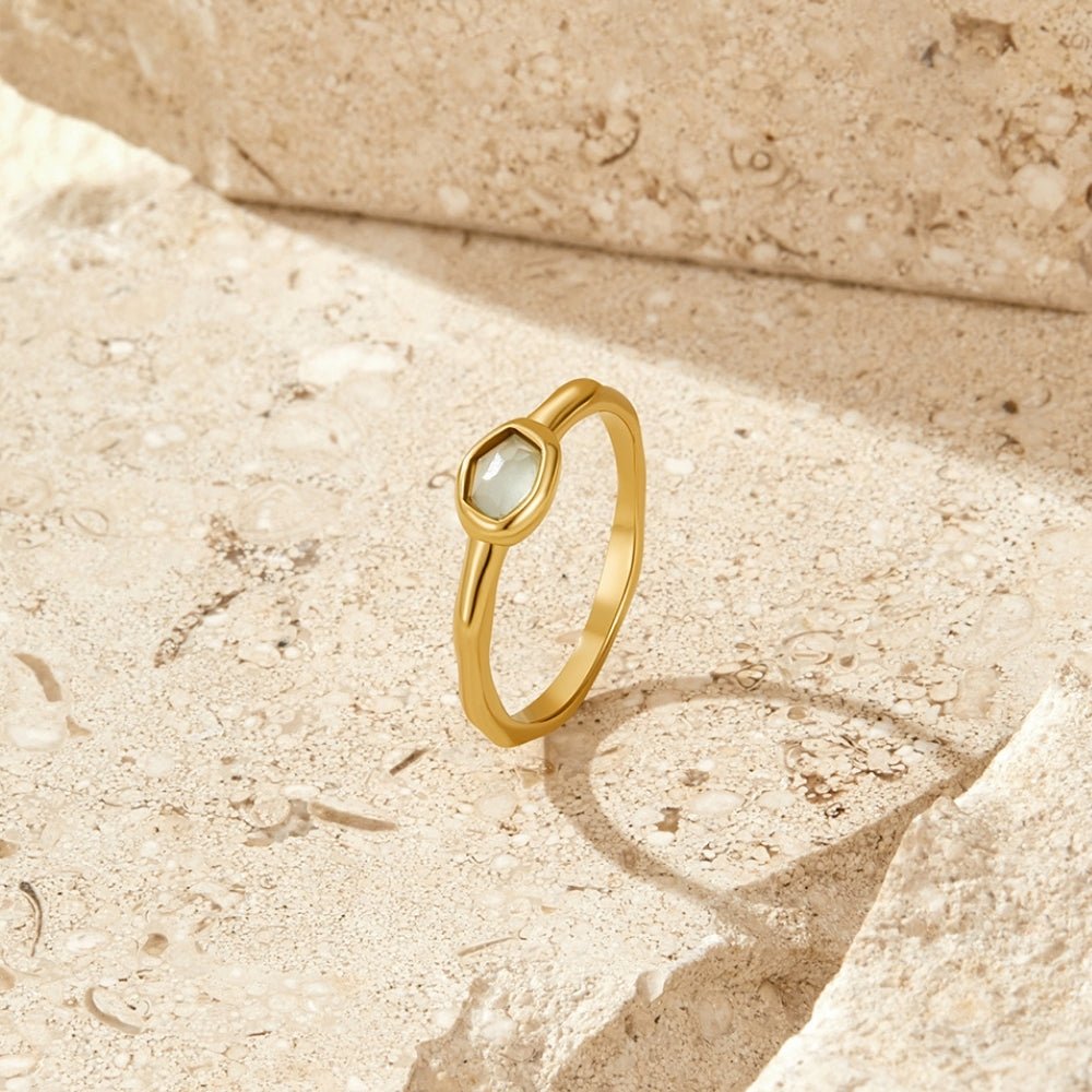 Selene Gold Moonstone Ring, standing upright on pale stone, gold band with a pale green-grey gem