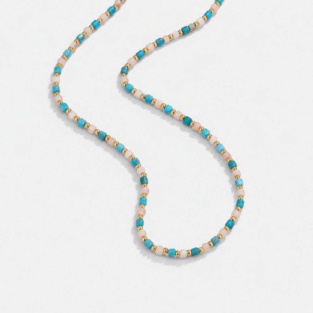 Alashan Blue Bead Necklace, laid flat on a pale grey surface in a loose S-curve, turquoise, pink and gold beads