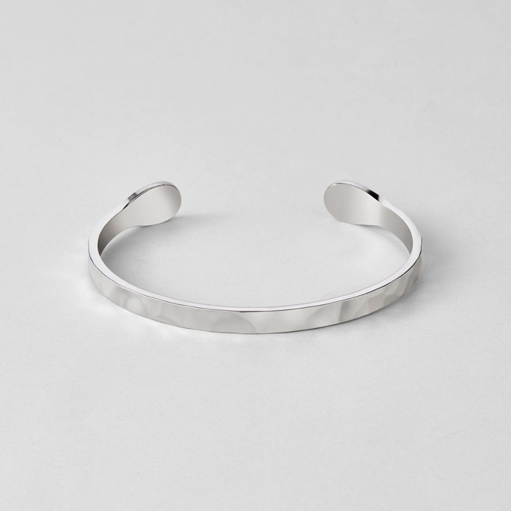Silver Alexa Bangle, open cuff bangle on a plain light grey surface, hammered texture
