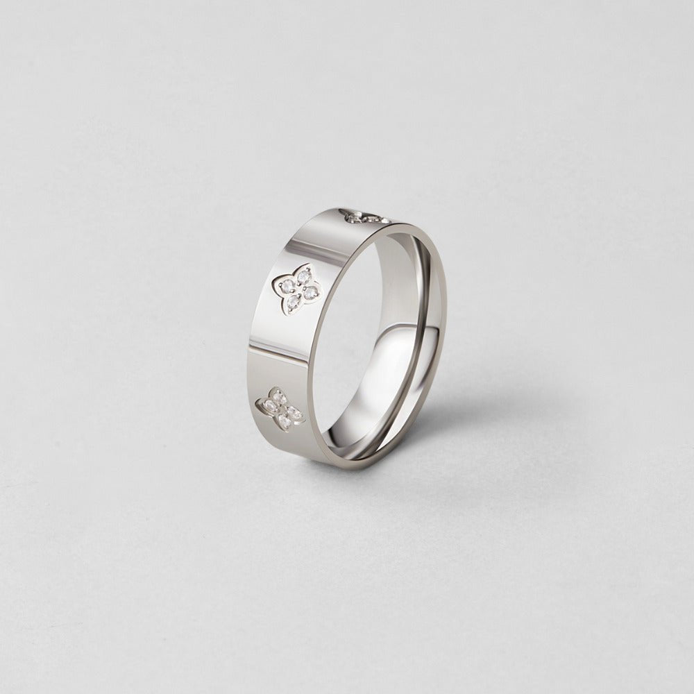 Silver Crystal Clover Band Ring, standing upright on a plain grey surface, polished silver