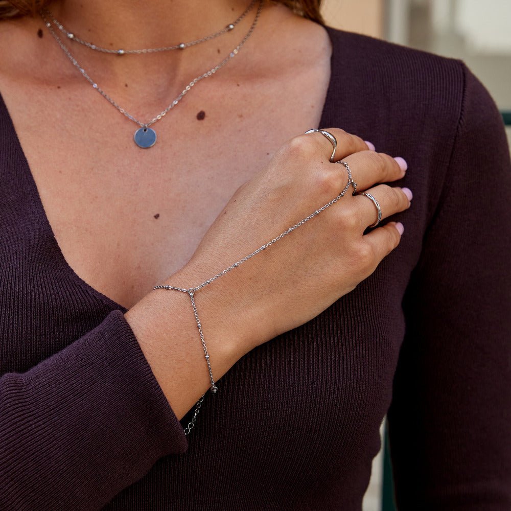 Silver Hand Chain Bracelet, worn on a hand with rings and a layered necklace