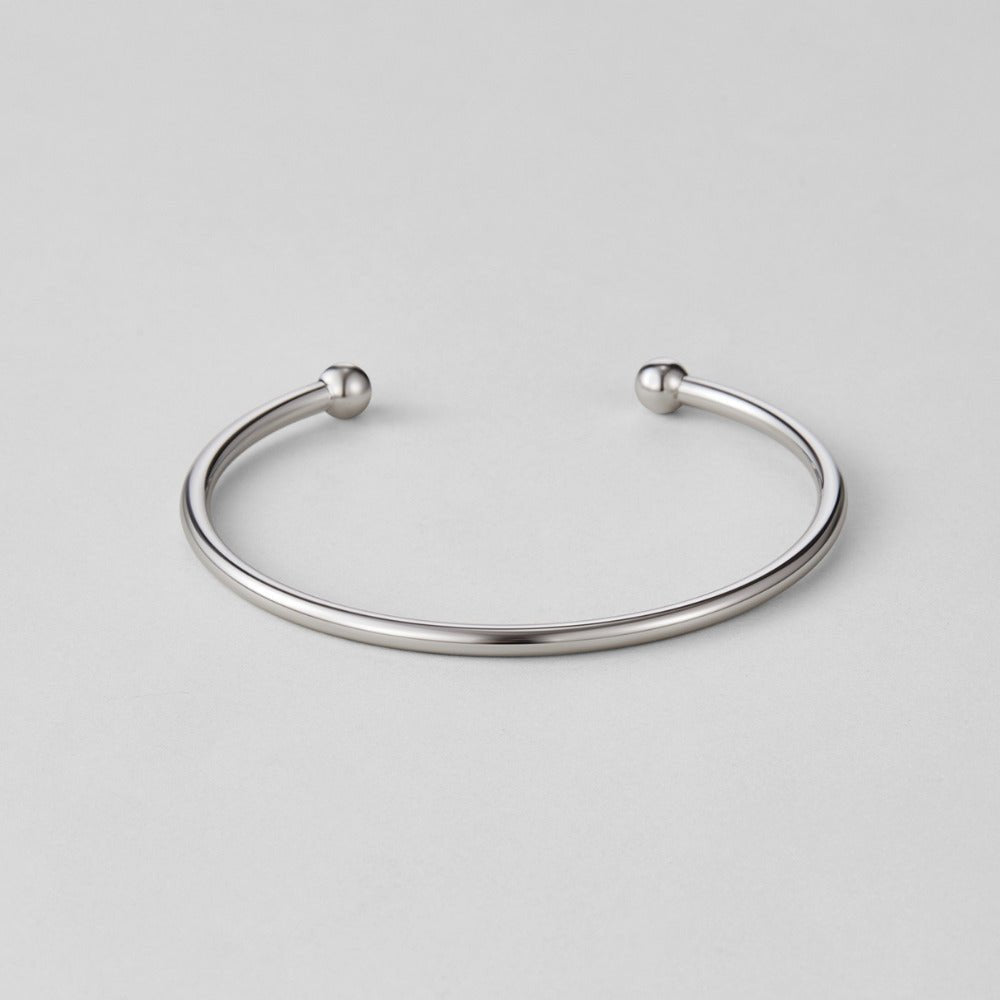 Silver Penelope Bangle, open cuff bangle with ball ends, lying flat on grey