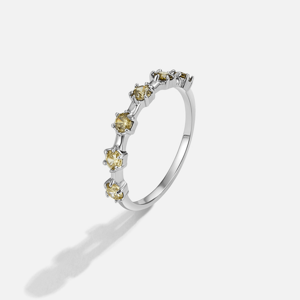 Silver Solana Crystal Ring, silver band with a row of yellow stones, standing upright on white