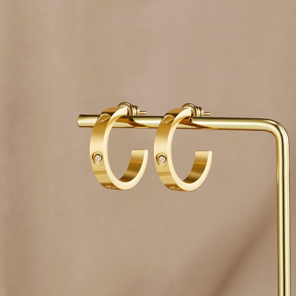 'Small Love' Hoop Earrings, a pair of gold hoops hanging on a gold display stand, with small