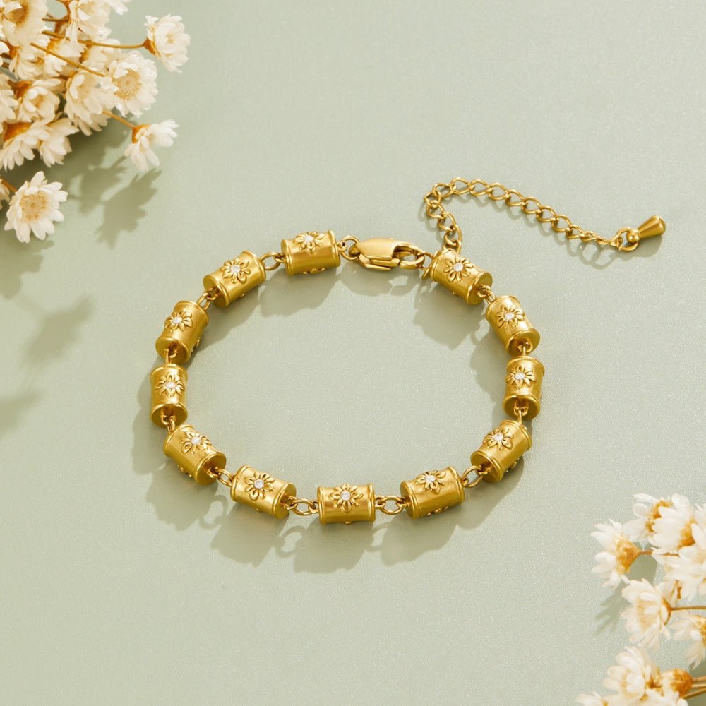 Stellar Gold Barrel Bracelet, laid flat on a sage surface beside dried white flowers