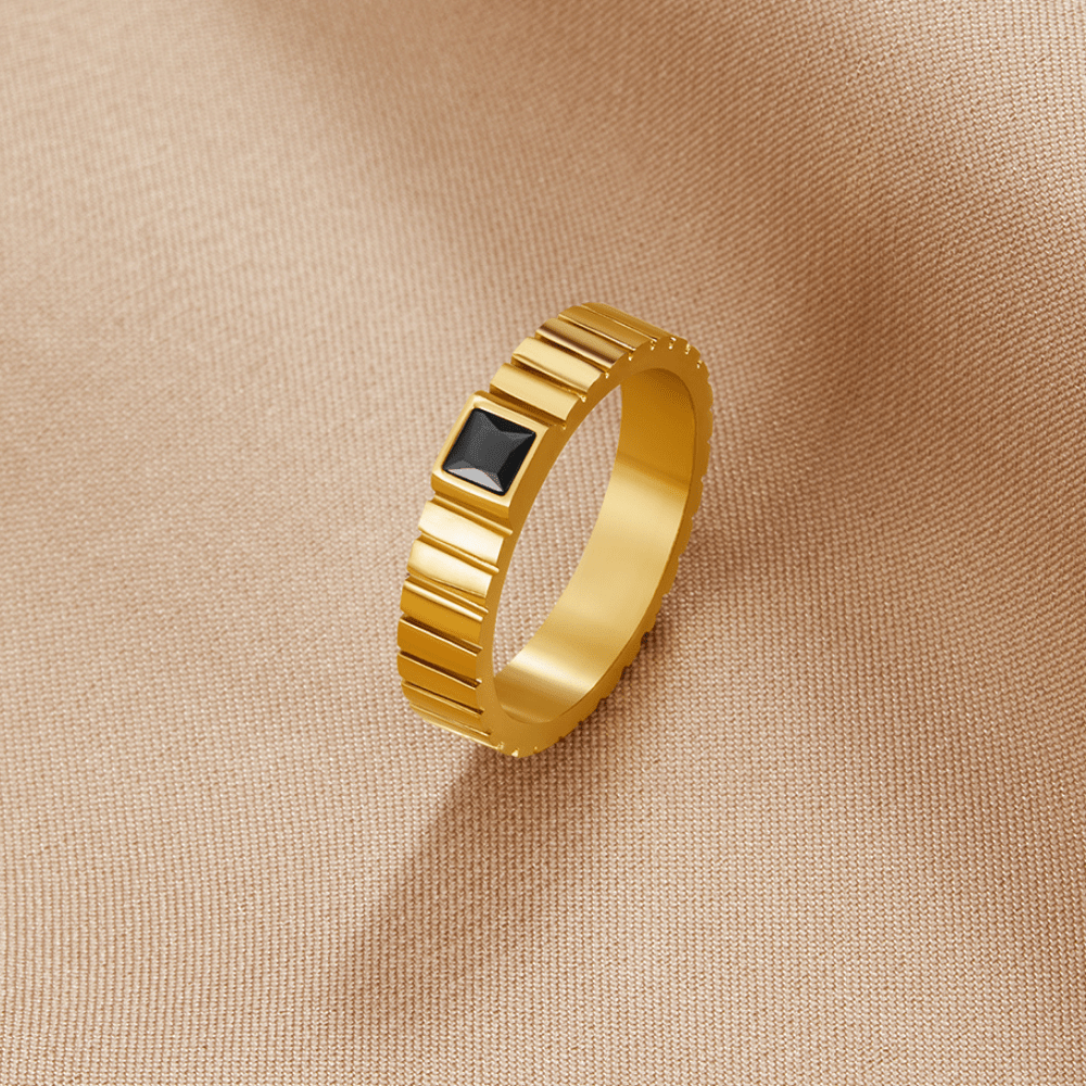 Talia Black Gold Ring, gold band with ridged edges and a square black stone, on beige fabric