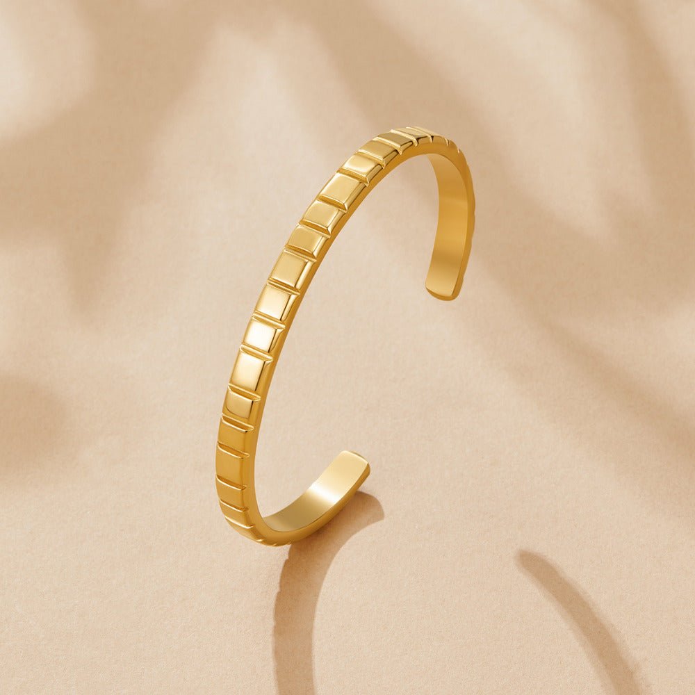 Tasha Ribbed Gold Bangle, open cuff bangle lying on a beige surface, segmented gold texture