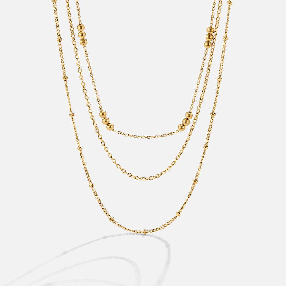 Tessa Triple Layered Necklace, three gold chains layered at different lengths on a white background
