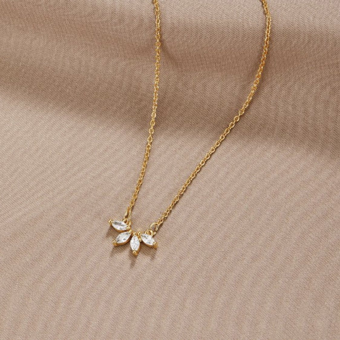 Tiffany Crystal Leaf Pendant Necklace, laid flat on beige fabric, gold chain with five pointed