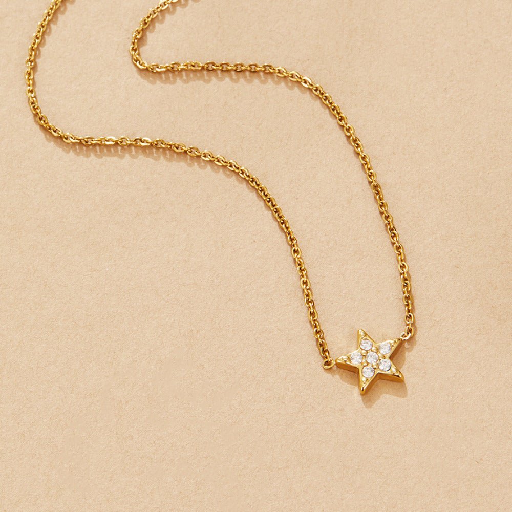 Tiny 'Shooting Star' Necklace, laid flat on a beige surface, gold chain with pavΓ© star pendant