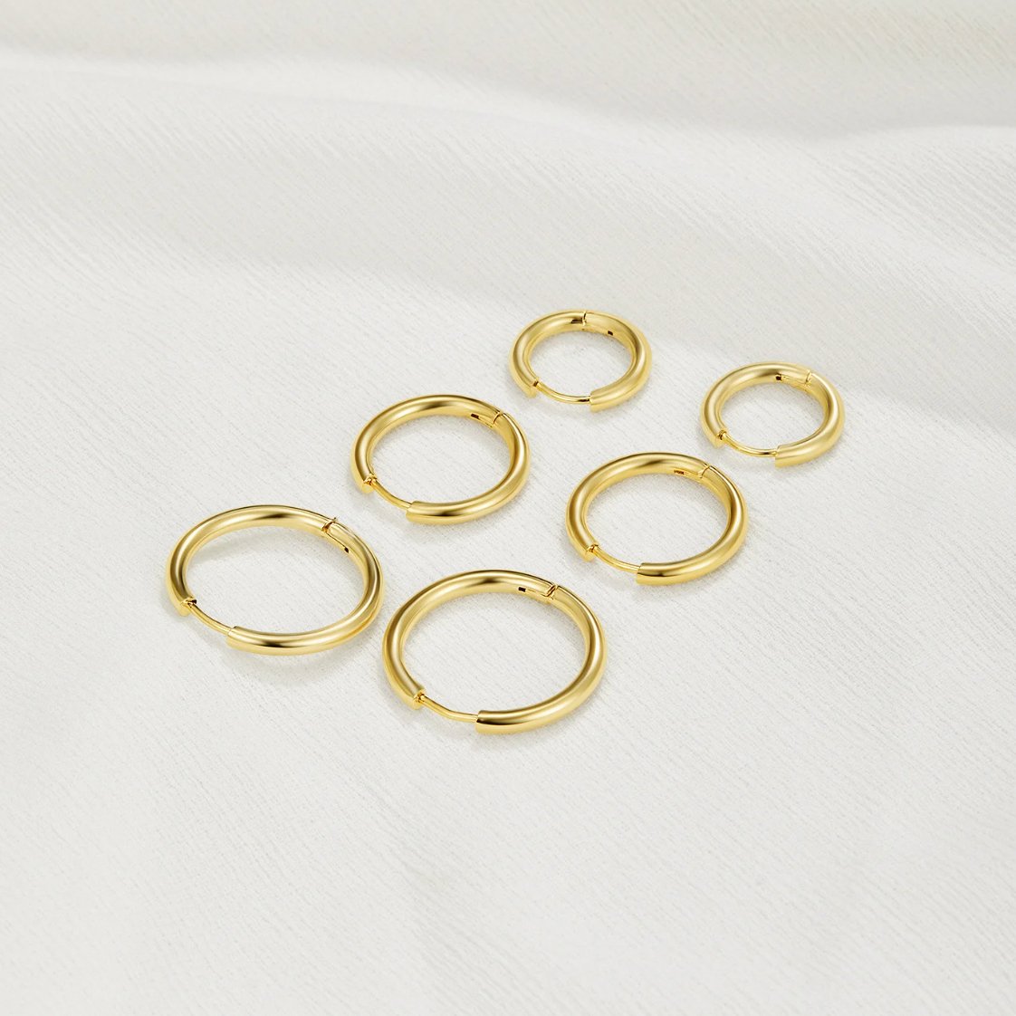 Triple Hoop Earrings Set, six gold hoop earrings in three sizes on white fabric