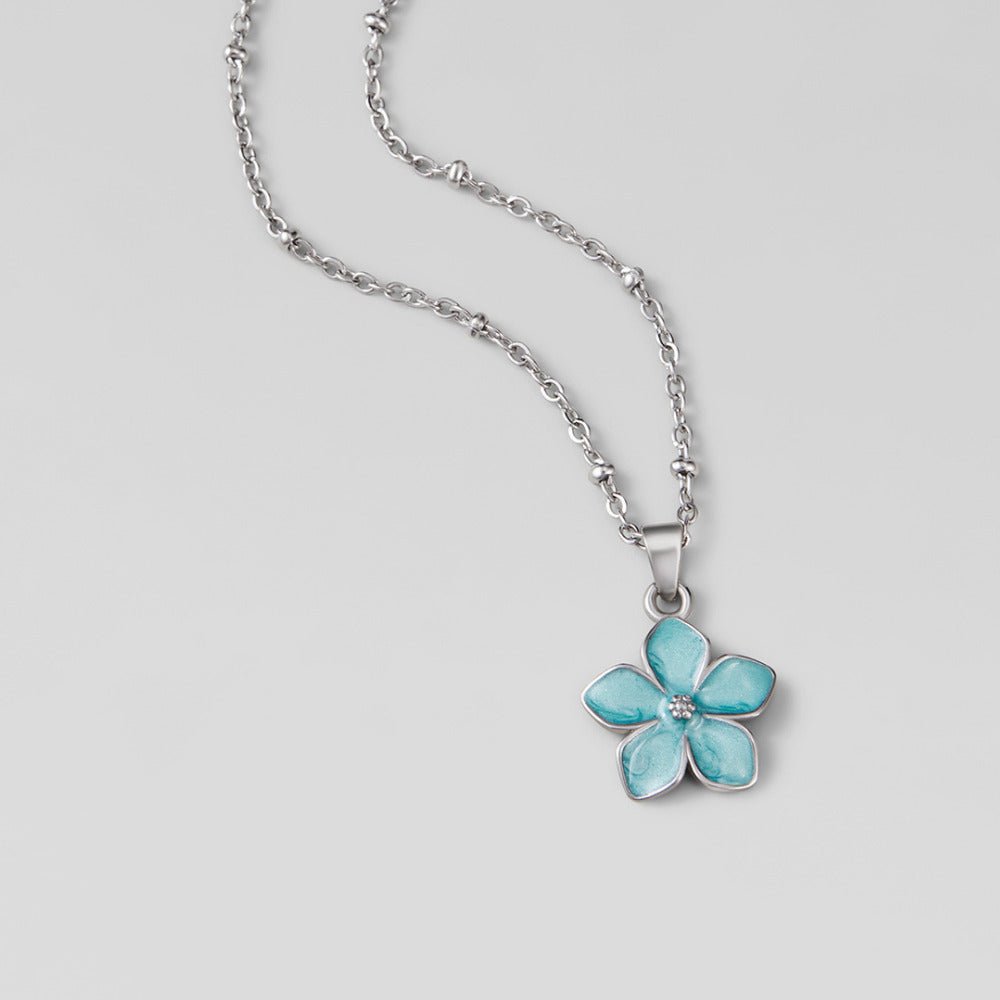 Turquoise Sakura Bloom Silver Necklace, lying flat on grey, silver chain with blue flower