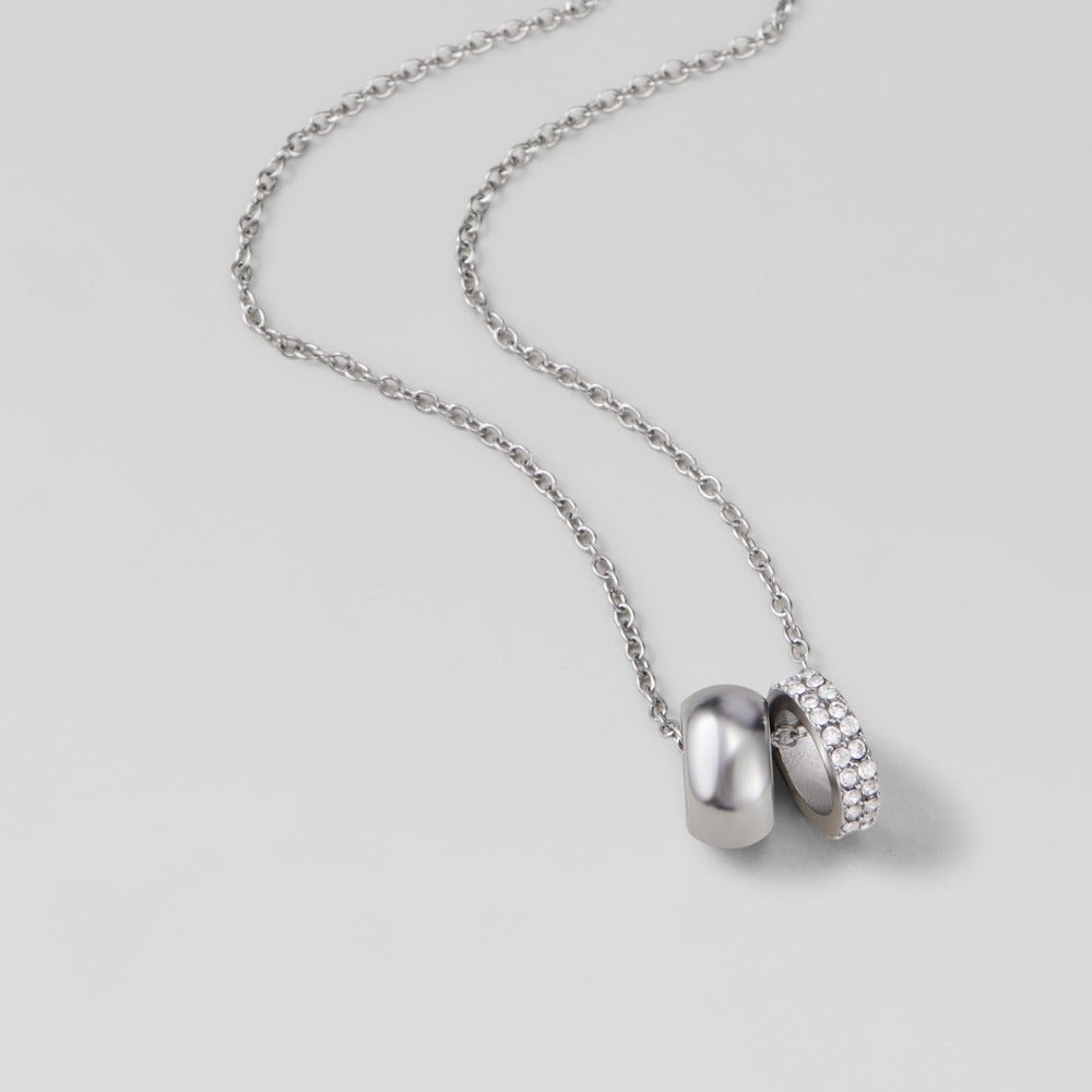 Twin Silver & Crystal Ring Pendant Necklace, laid flat on grey, plain and crystal-set rings on