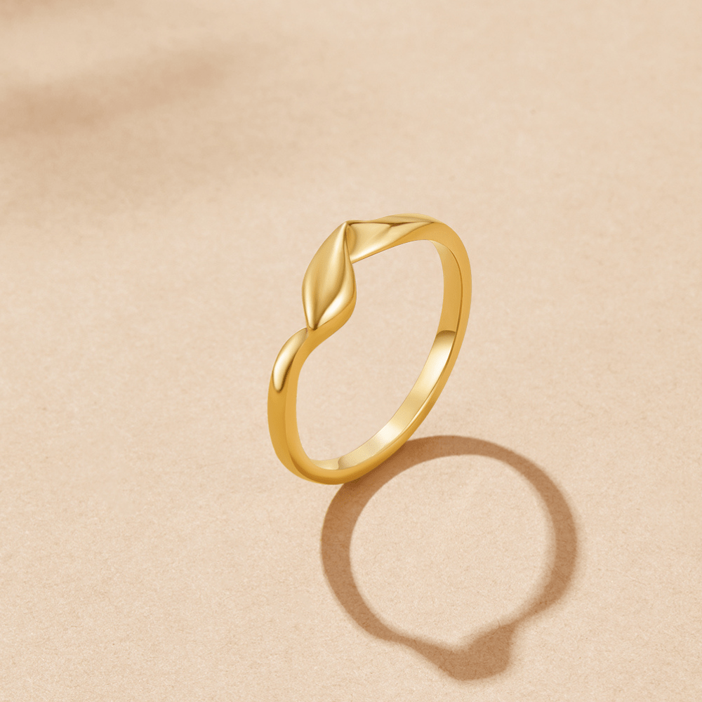 Twisted Athena Gold Ring, gold ring standing upright on beige surface, casting a shadow