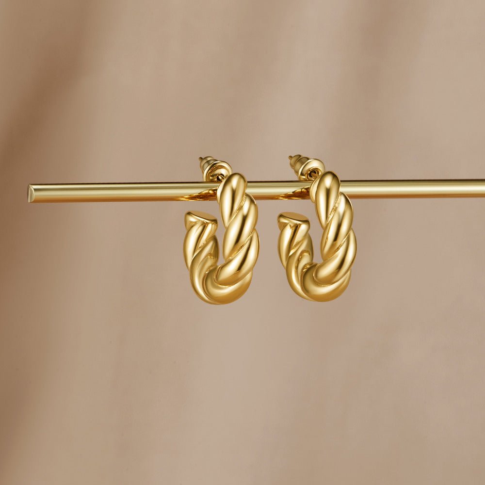 Twisted Felicity Hoop Earrings, pair of twisted gold hoops hanging from a gold bar on beige fabric
