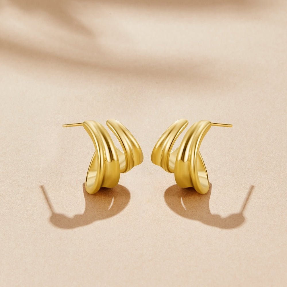 Twisted Ivana Hoop Earrings, a pair of polished gold earrings on a beige surface, shown flat