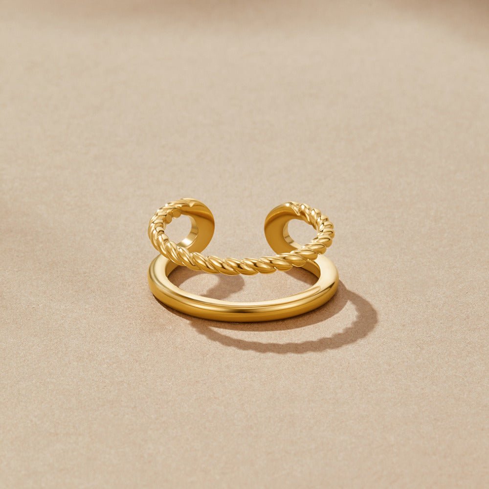 Twisted Tyra Gold Ring, lying flat on sand-coloured surface, twisted and smooth gold bands