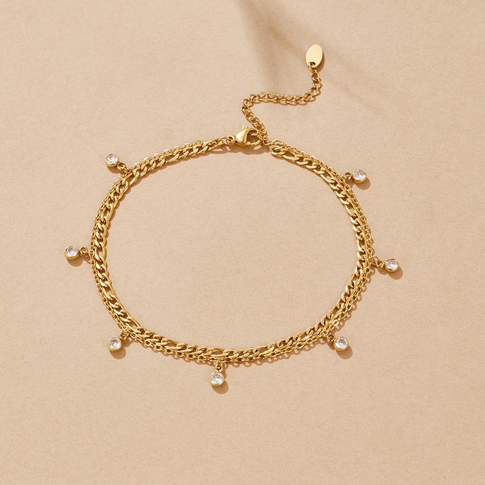Vera Gold & Crystal Layered Anklet, flat lay of a double gold chain with six dangling crystal drops on beige