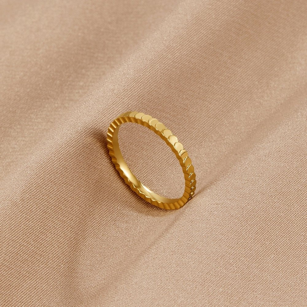 Vera Gold Ring, gold band ring lying on a beige satin fabric, scalloped edge visible