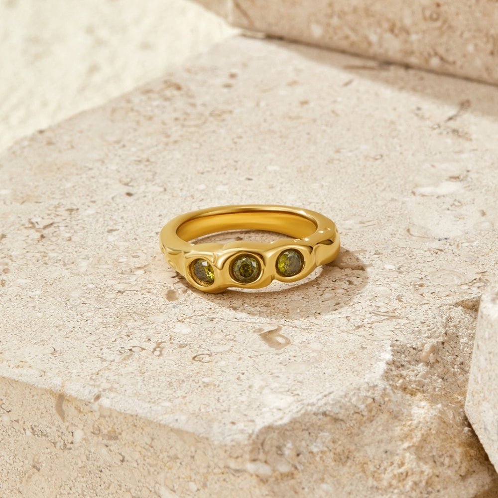 Vintage Peridot Gold Ring, gold ring with three green stones, resting on pale stone