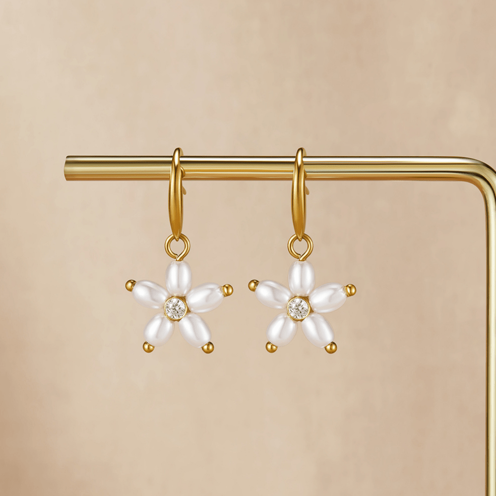 White Flower Pearl Drop Earrings, a pair of earrings hanging on a gold display stand against beige