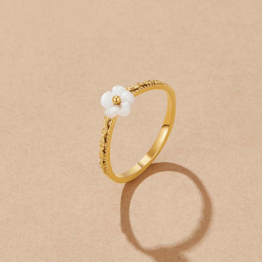 White Petal Shell Ring, gold band with a white flower-shaped shell on a beige surface