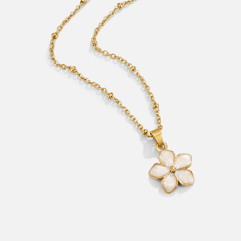 White Sakura Bloom Gold Necklace, laid flat on a pale grey surface, gold chain with a white