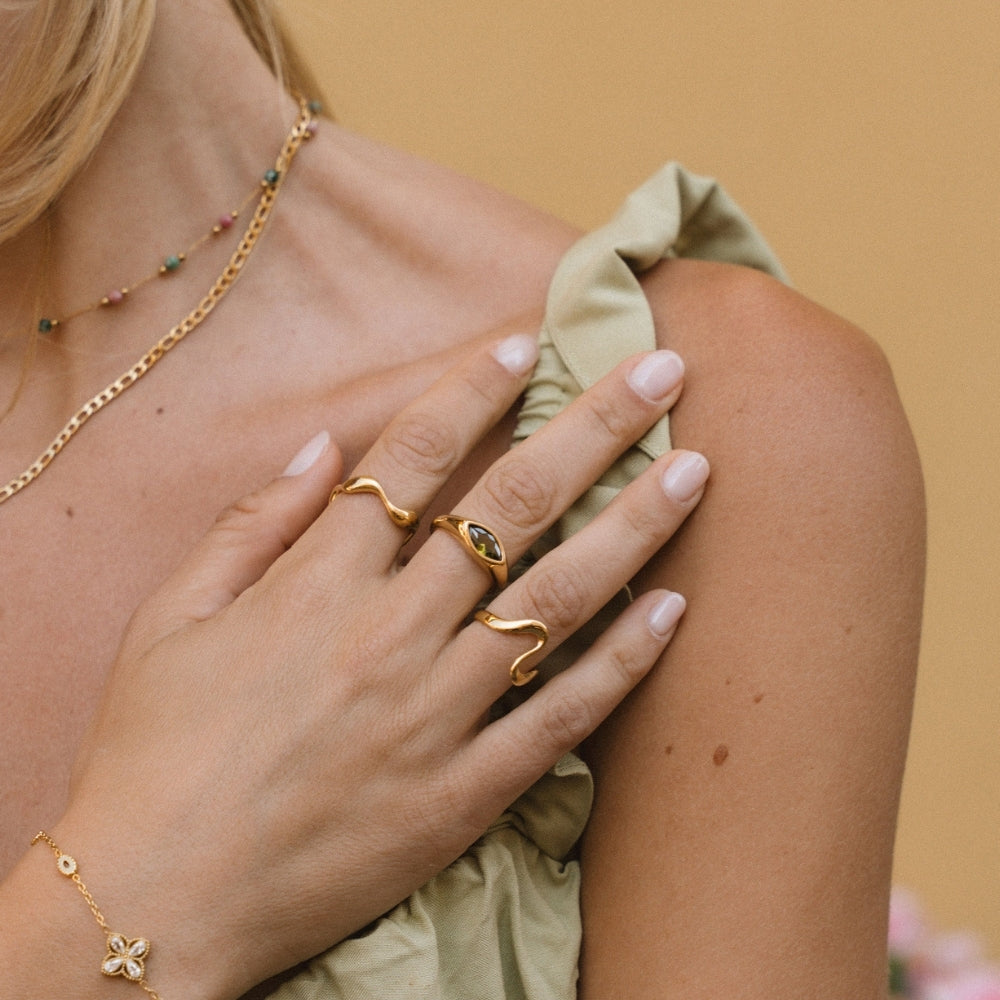 Gold Wave Ring, worn on a hand with a green-stone ring and gold necklaces