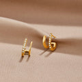 18K Gold & Crystal Claw Earrings, a pair of gold earrings lying on a beige satin cloth, one crystal-set