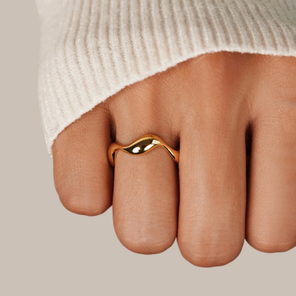 18K Gold Wave Ring, worn on a hand in a cream knit sleeve, polished gold band