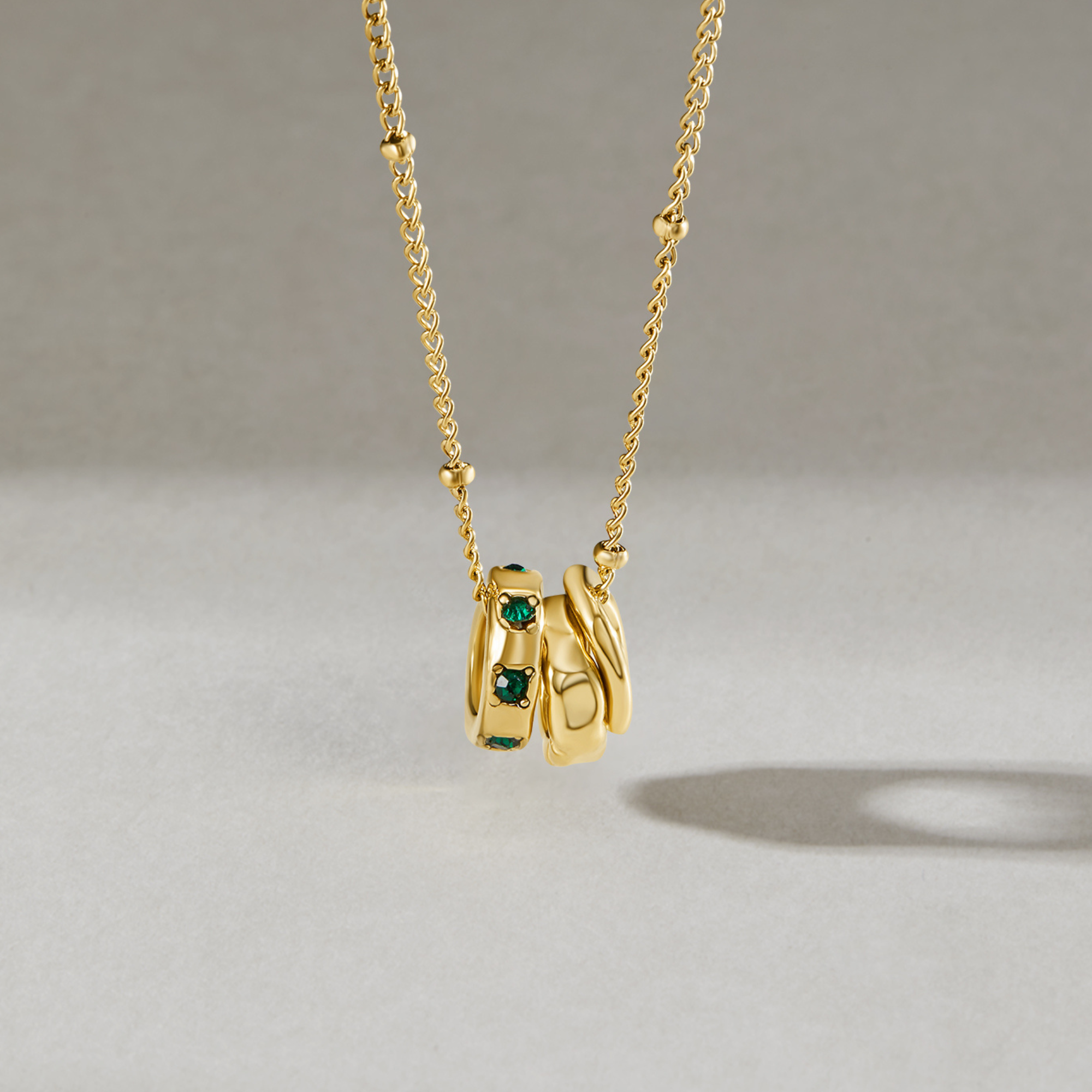Camilla Pendant Necklace, hanging on a fine gold chain against a grey backdrop