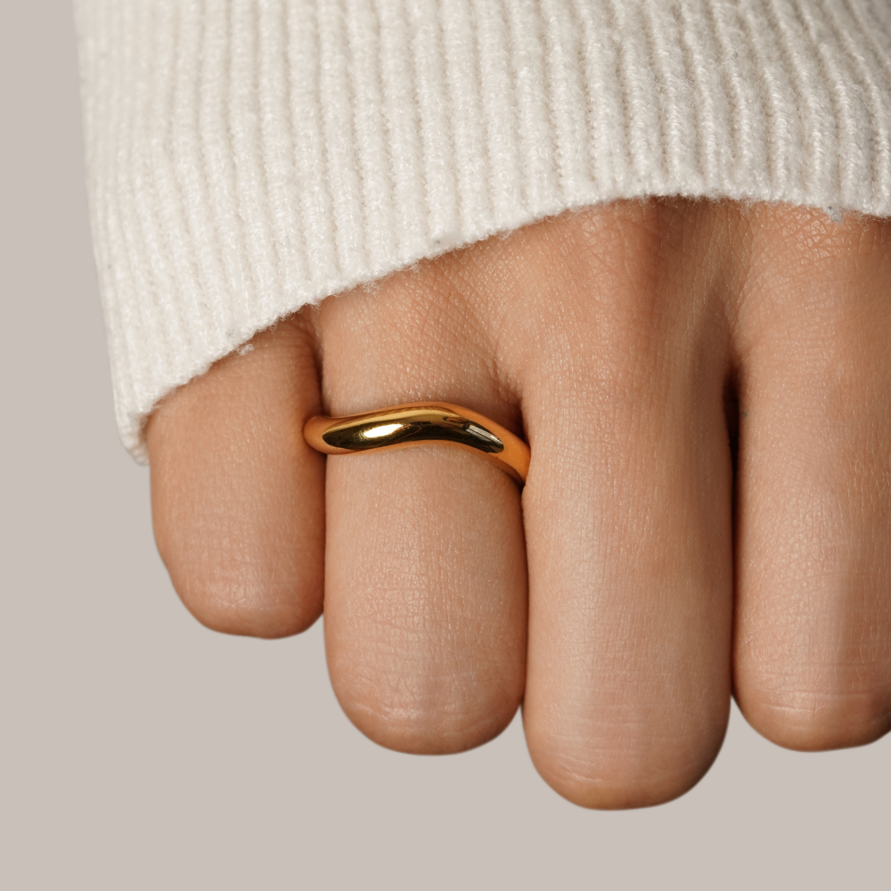 Mina Gold Wave Ring, worn on a finger below a cream knit sleeve, polished gold