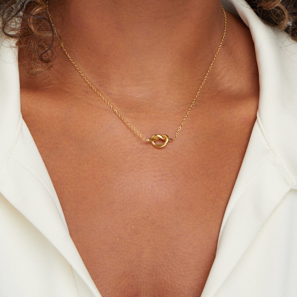 Adela Knot Necklace, worn on a neck with a white open-collar shirt, gold knot pendant