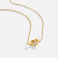 Adela Knot Necklace, gold chain necklace laid flat on a pale background, with a knot pendant